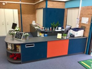 Circulation desk at Robert Townsend Public School with Ironstone cabinetry, display corner cabinets, and book return with Octane and Burnt Orange pinboards